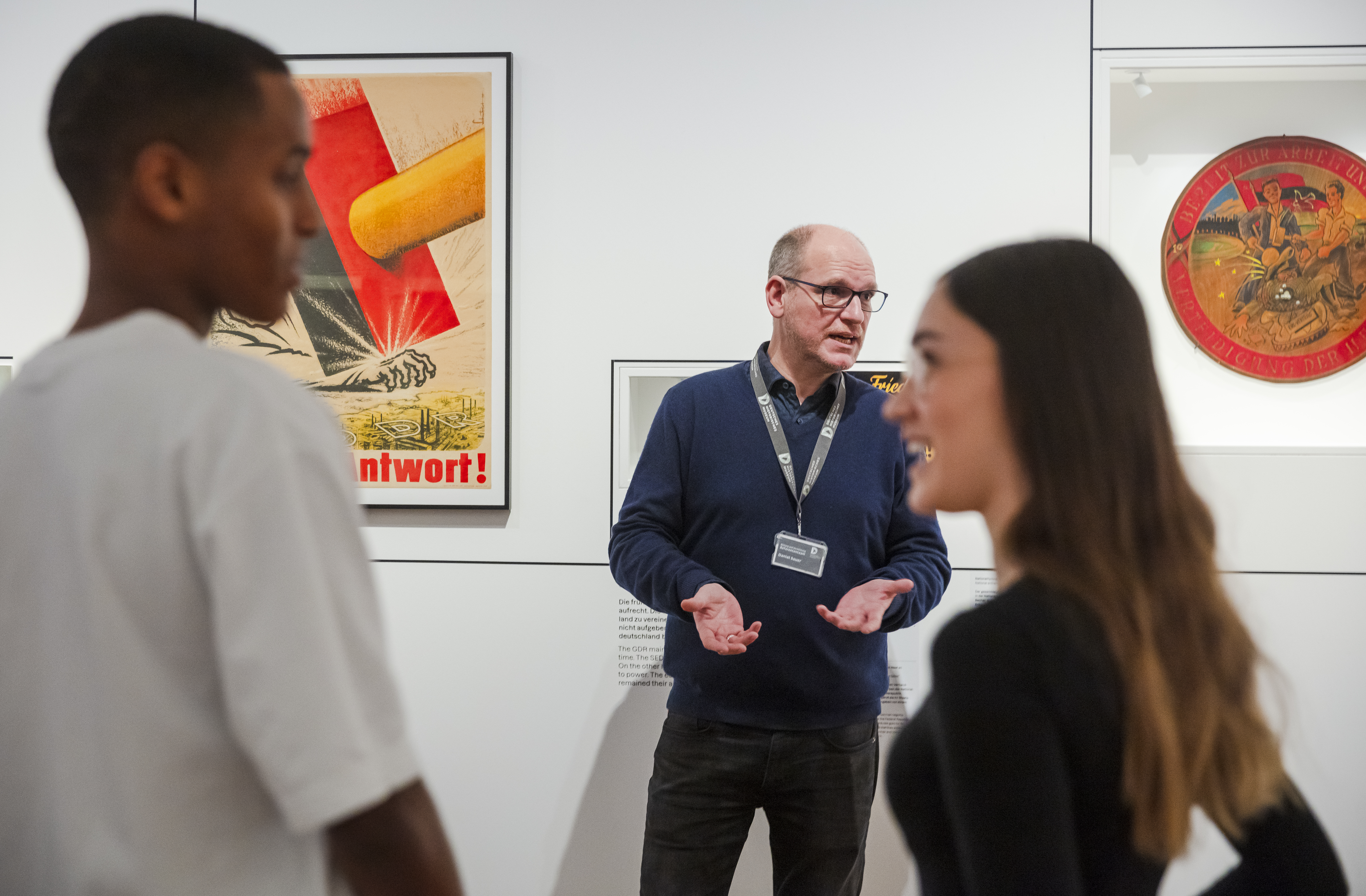 Ein Mann gibt eine Führung und steht vor einer Ausstellungswand.