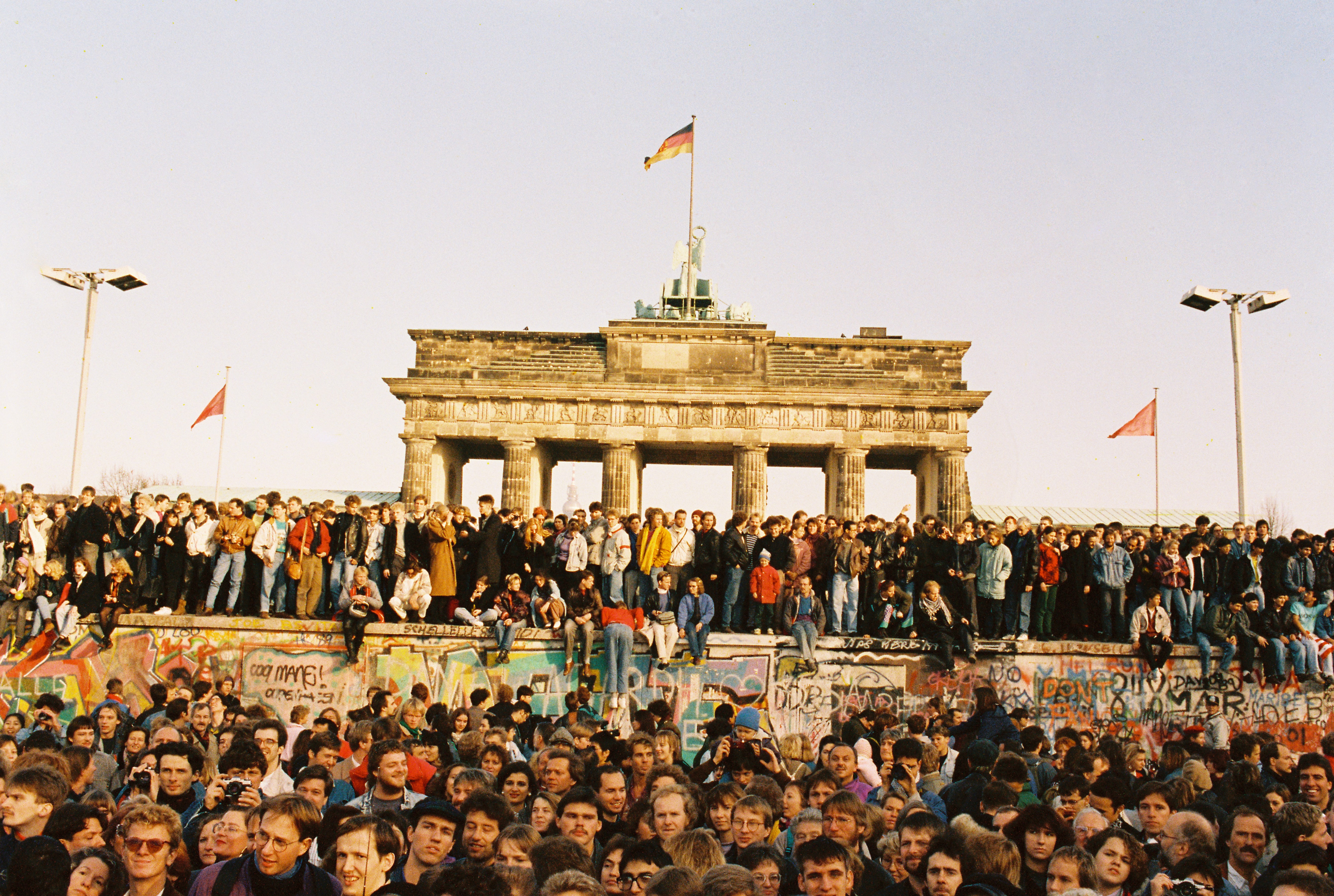 Menschen stehen vor und auf der Berliner Mauer und im Hintergrund ist das Brandenburger Tor.