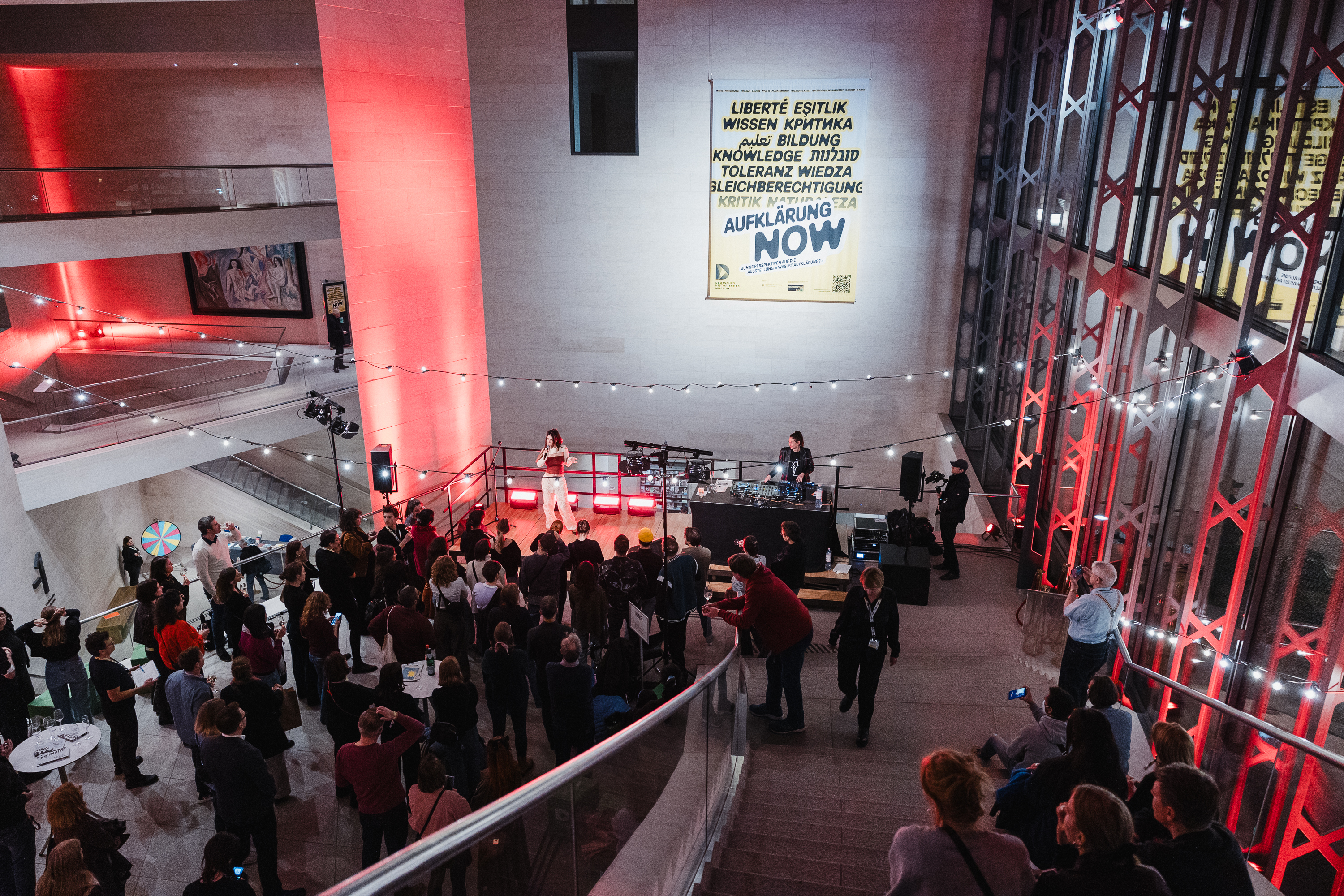 Aufklärung NOW Festival im Deutschen Historischen Museum Viele Menschen stehen und sitzen im Foyer eines Museums und schauen sich ein musikalisches Bühnenprogramm an.