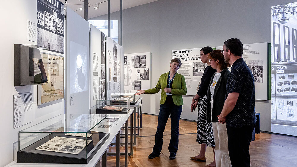 Personen stehen in einer Ausstellung und hören einer Referentin zu