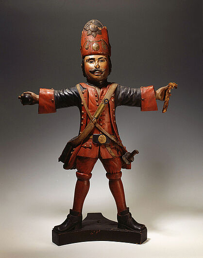 Ein Grenadier – Figur zur Tabakaufbewahrung, 1715.  Die Figur in der Uniform eines Riesengrenadiers erinnert an die Lieblingsgarde König Friedrich Wilhelms I. Die Mütze des Grenadiers ist abnehmbar. Das Kopfinnere diente als Behältnis für Tabak. (Inv.Nr. U 2492)