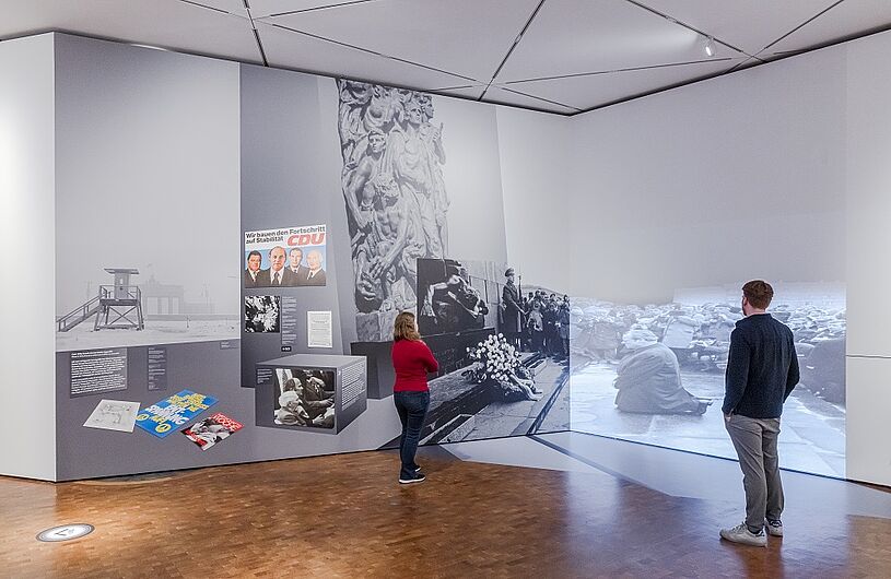 Besucher betrachten Ausstellungsstücke und Wandbilder in einem modernen Museum.
