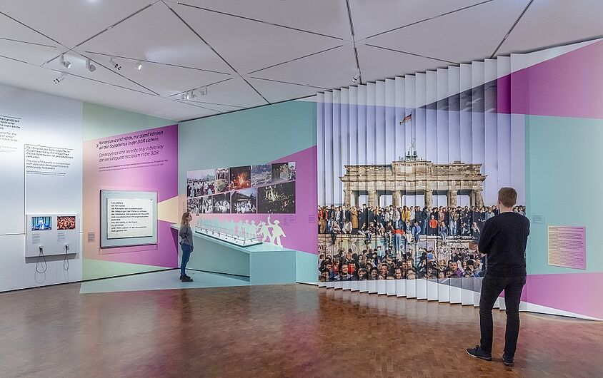 Zwei Personen betrachten eine moderne Museumsausstellung mit Texten und Wandbildern.
