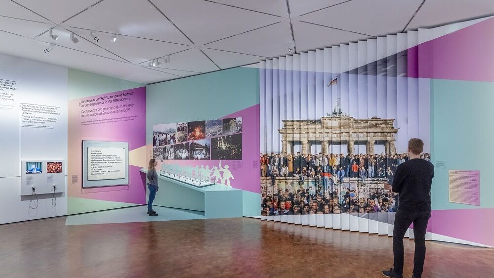 Zwei Personen betrachten eine moderne Museumsausstellung mit Texten und Wandbildern.