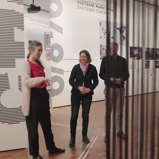 Drei Leute stehen vor einer Ausstellungswand und reden miteinander.