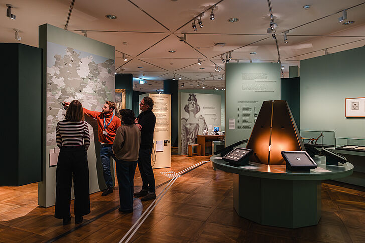 Exhibition view "Nature and German History. Faith – Biology – Power" A man in a red sweater gives three visitors a guided tour.
