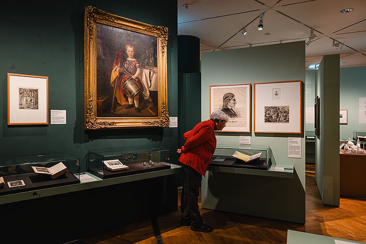 Exhibition view "Nature and German History. Faith – Biology – Power" A woman in a red jacket looks at a book.