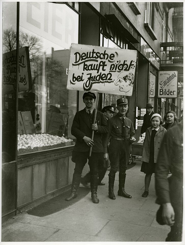 Ein Mann hält ein Plakat "kauft nicht bei Juden" in der Hand.