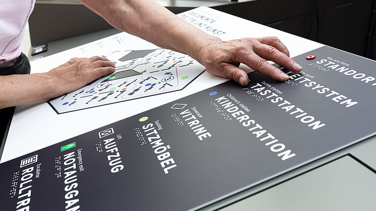 Eine Tafel mit Blindenschrift wird von einer Person benutzt.