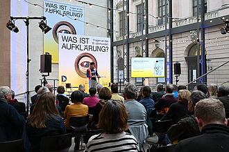 Ein Mann steht auf der Bühne vor dem Publikum.