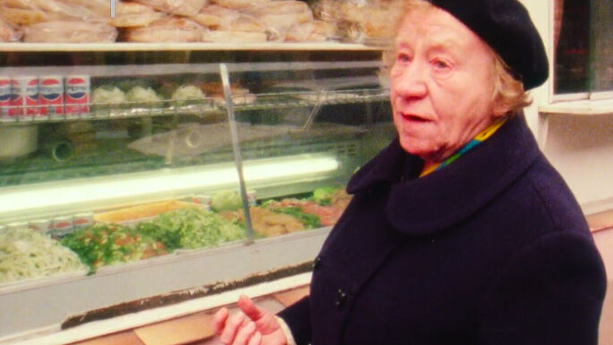 Eine Dame steht vor einer Theke mit Essen und spricht.