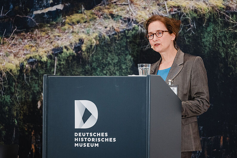 Viktoria Urmersbach steht an einem Pult und spricht zum Publikum.