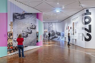 Mehrere Personen betrachten eine bunte, moderne Ausstellung in einem Museumsraum.
