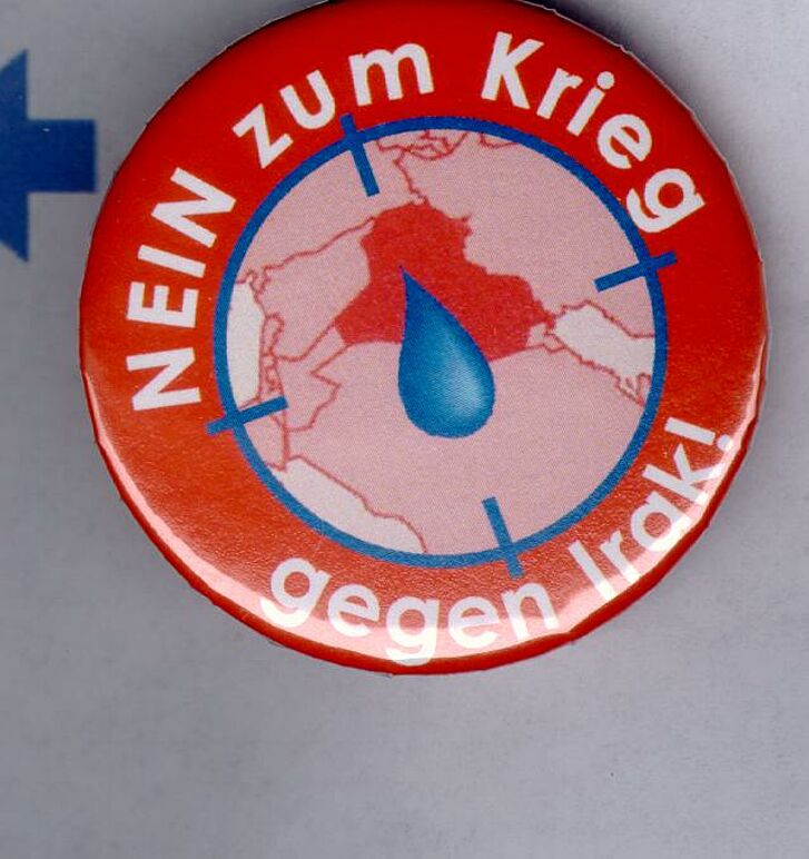Roter Button mit Text "Nein zum Krieg gegen Irak" und Karte mit Tropfen in der Mitte.
