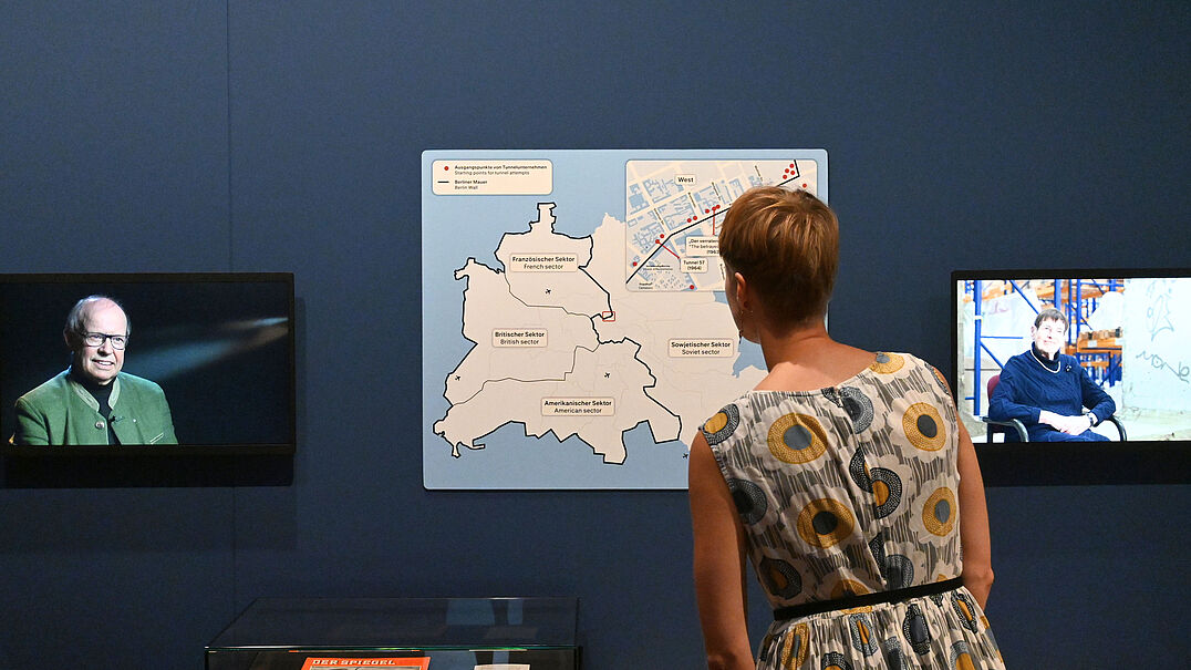 Eine Person steht in einer Ausstellung und betrachtet eine Karte zum Verlauf der Berliner Mauer.
