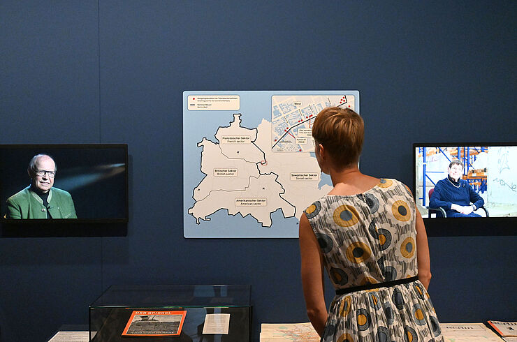 Eine Person steht in einer Ausstellung und betrachtet eine Karte zum Verlauf der Berliner Mauer.