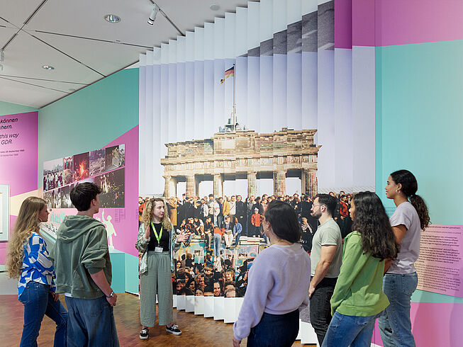 Ausstellungsansicht „Roads not Taken. Oder: Es hätte auch anders kommen können“ Führungssituation mit einem weiblichen Guide und einer Traube von sechs Personen in der Ausstellung