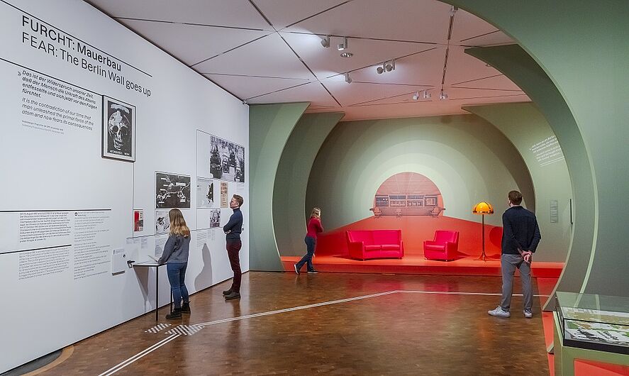Besucher betrachten Ausstellungsstücke und Wandbilder in einem modernen Museum.
