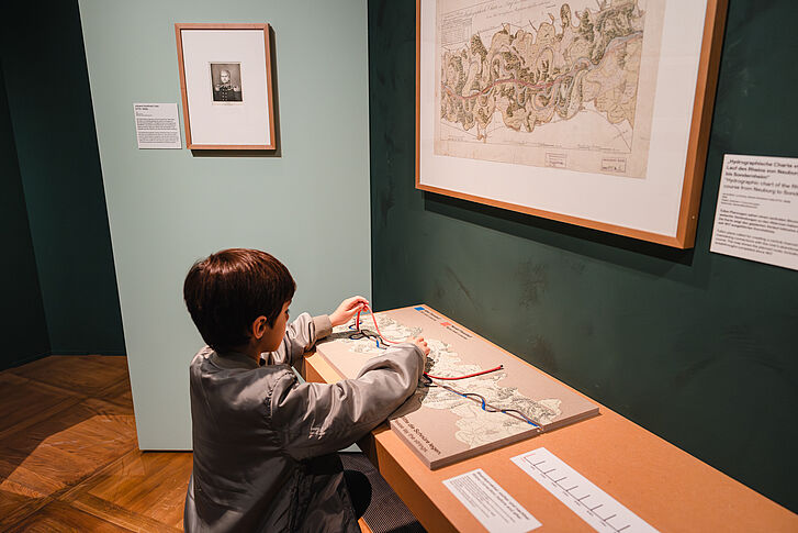 Exhibition view "Nature and German History. Faith – Biology – Power" A boy is sitting at an interactive station and holding a red cord in his hand.