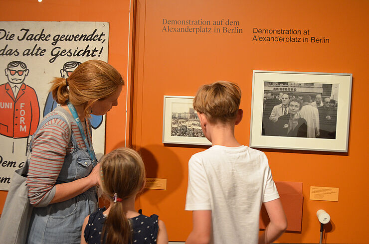 Kinderführung "Warte nicht mit deinem Mut!" Eine Frau und zwei Kinder sehen sich eine Fotographie an.