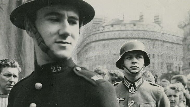 Viele Menschen und zwei Soldaten stehen auf einer Straße.