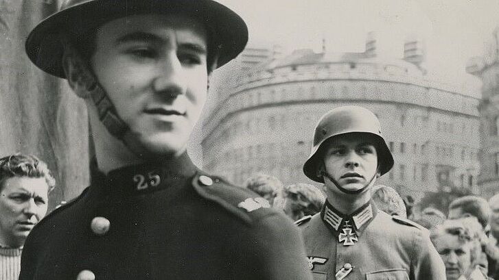 Viele Menschen und zwei Soldaten stehen auf einer Straße.