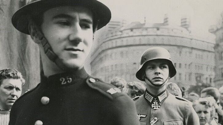 Viele Menschen und zwei Soldaten stehen auf einer Straße.