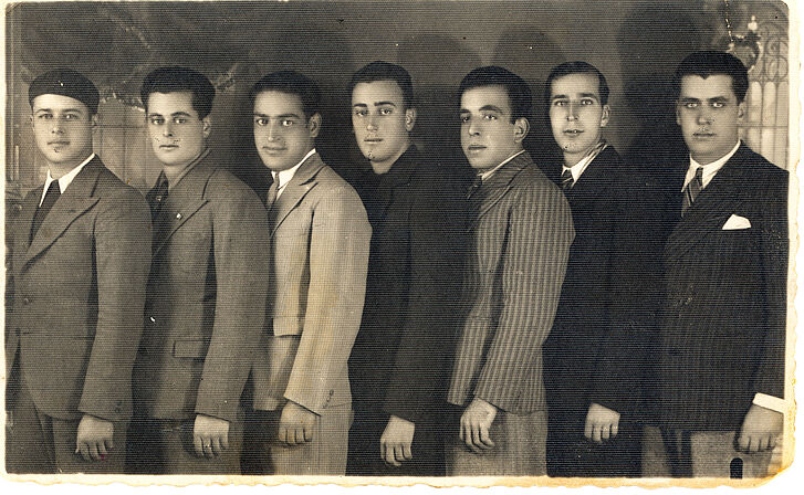 The picture shows a black-and-white photograph of seven men in suits.