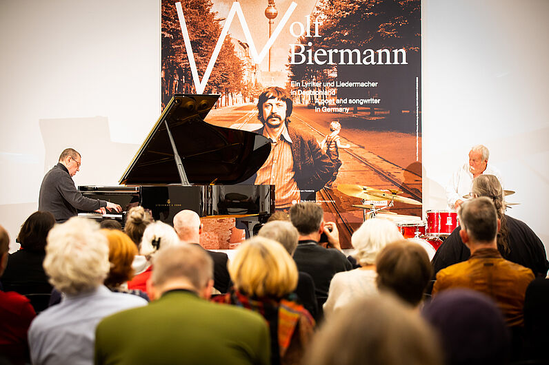 Zwei Männer spielen Klavier und Schlagzeug vor Publikum.