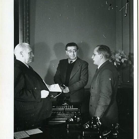 Wilhelm Pieck, Leo Zuckermann und Otto Winzer blicken sich an und sprechen miteinander.