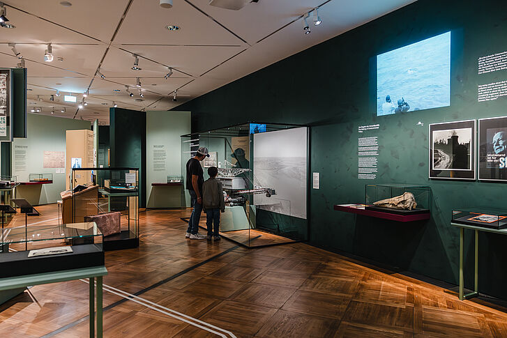 Exhibition view "Nature and German History. Faith – Biology – Power" Father and son look at an excavator