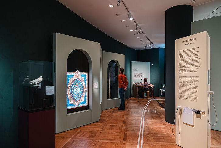 Ausstellungsansicht "Natur und deutsche Geschichte. Glaube – Biologie – Macht" Ein Mann in einem roten Pullover und eine Frau in gestreiften Oberteil in der Ausstellung "Natur und deutsche Geschichte. Glaube – Biologie – Macht"