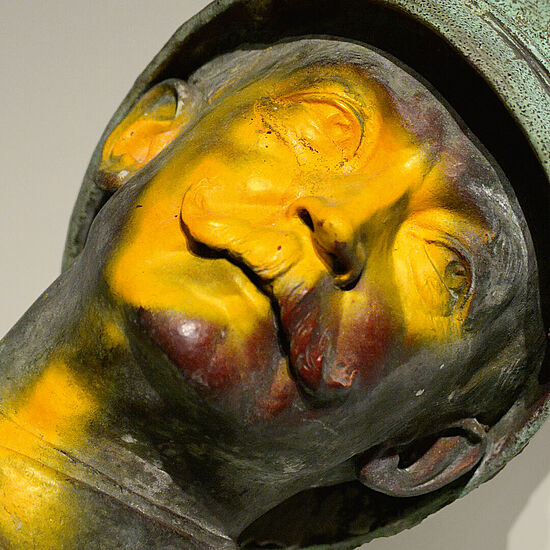 Kopf einer verfärbten Bronzeskulptur eines Mannes mit Bart und Helm.