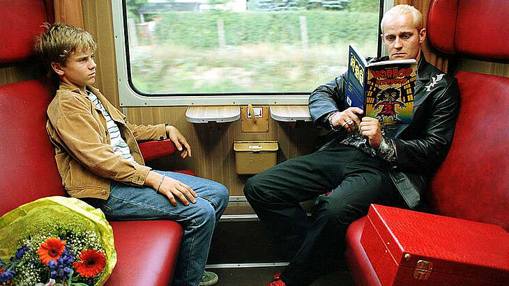 Ein Mann und ein Junge sitzen sich im Zug gegenüber.