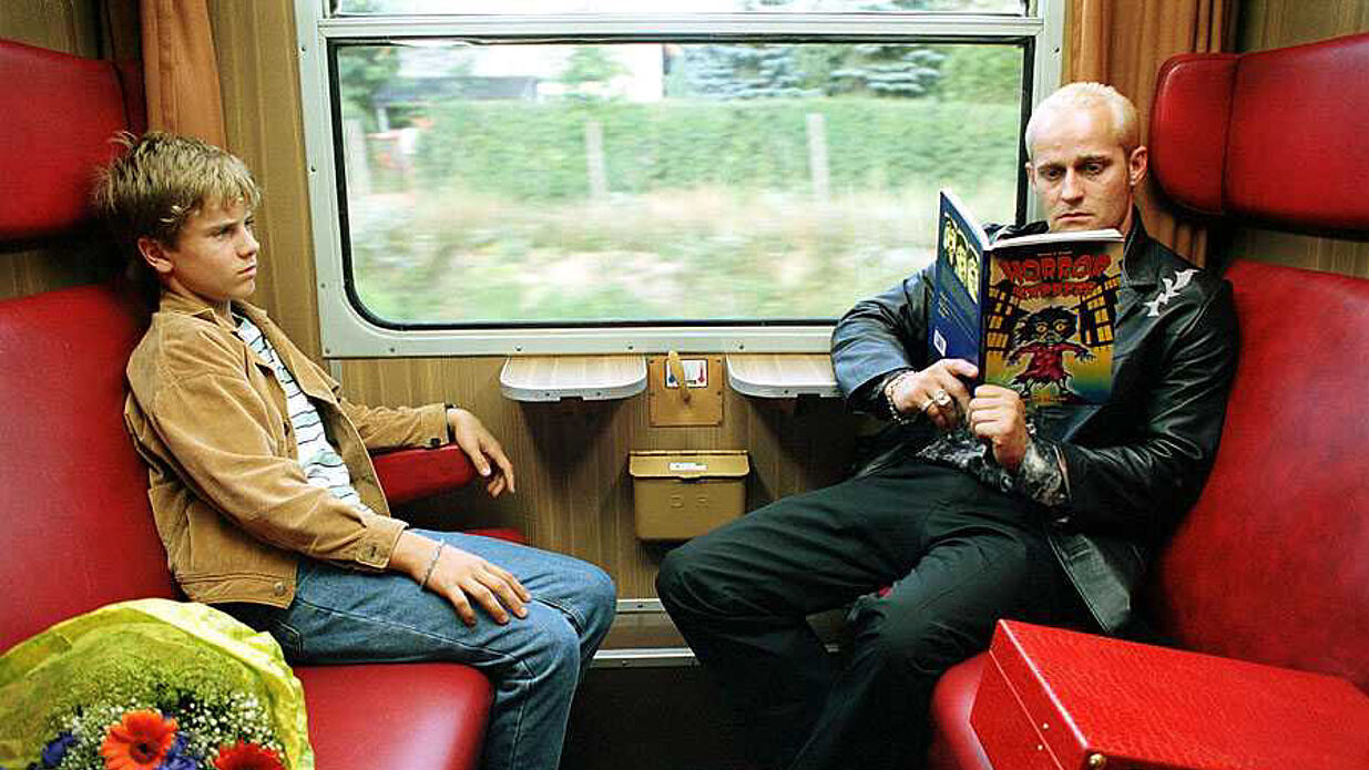 Ein Mann und ein Junge sitzen sich im Zug gegenüber.