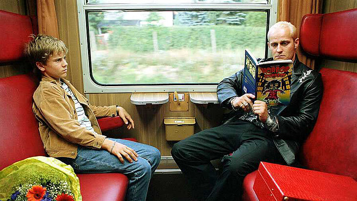 Ein Mann und ein Junge sitzen sich im Zug gegenüber.