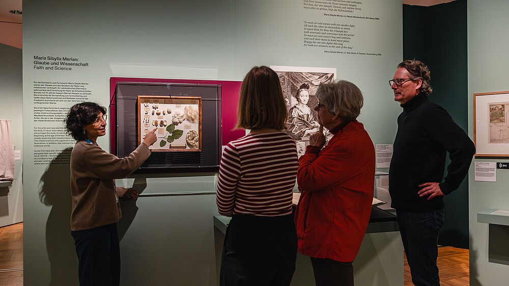 Personen stehen in einer Ausstellung und hören einer Referentin zu
