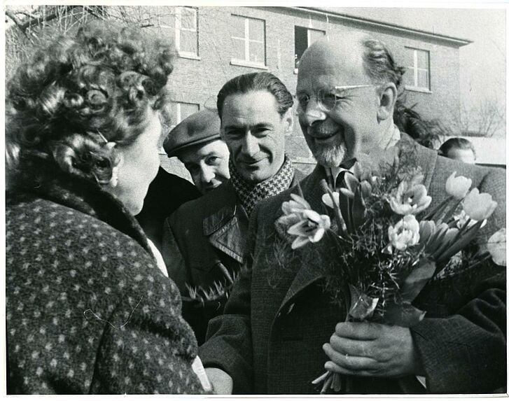 Ein Mann mit Blumen in der Hand spricht zu einer Frau.