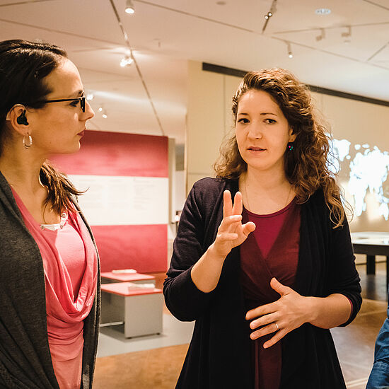 Eine Frau erklärt einer anderen Frau etwas in einem Ausstellungsraum.