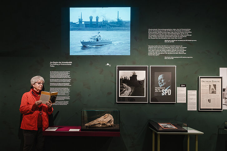 Exhibition view "Nature and German History. Faith – Biology – Power" A woman in a red jacket reads a book next to the skull of a beluga whale.