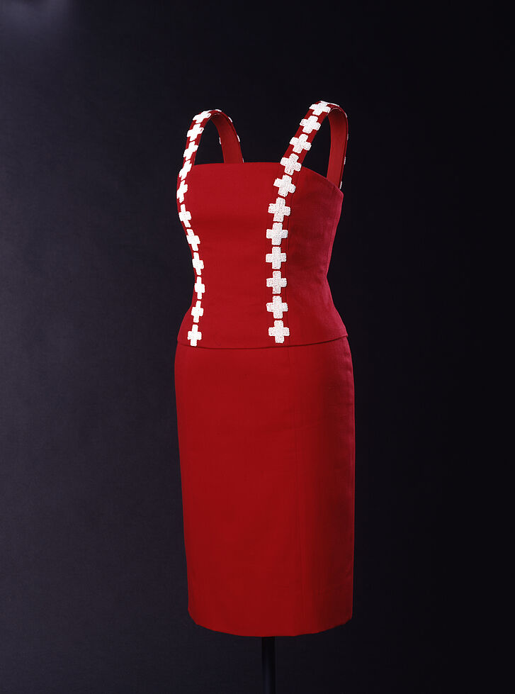 Ein rotes und eng anliegendes Kleid mit einer Leiste von weißen Kreuzen rechts und links.