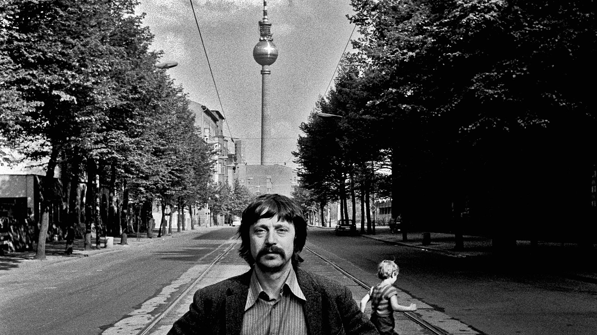 Wolf Biermann steht auf der Strasse und hinter ihm sieht man den Fernsehturm.
