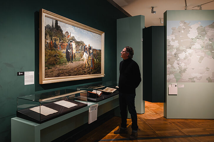Exhibition view "Nature and German History. Faith – Biology – Power" A man in a black sweater is looking at a painting.