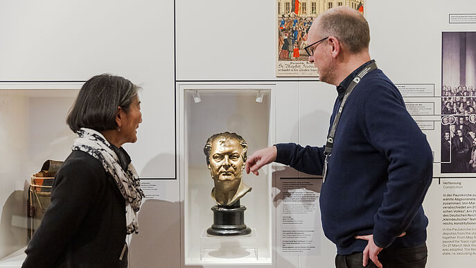 Eine Frau und ein Mann betrachten eine Büste eines Mannes.