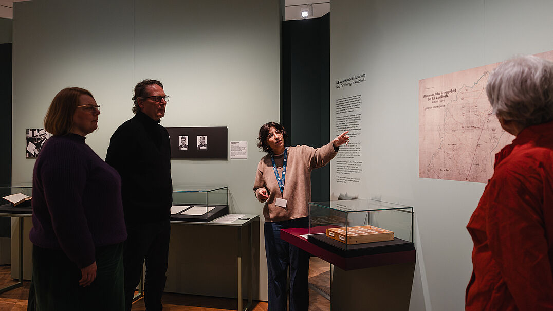 Mehrere Personen stehen in einer Ausstellung. Eine Person zeigt auf ein Objekt.