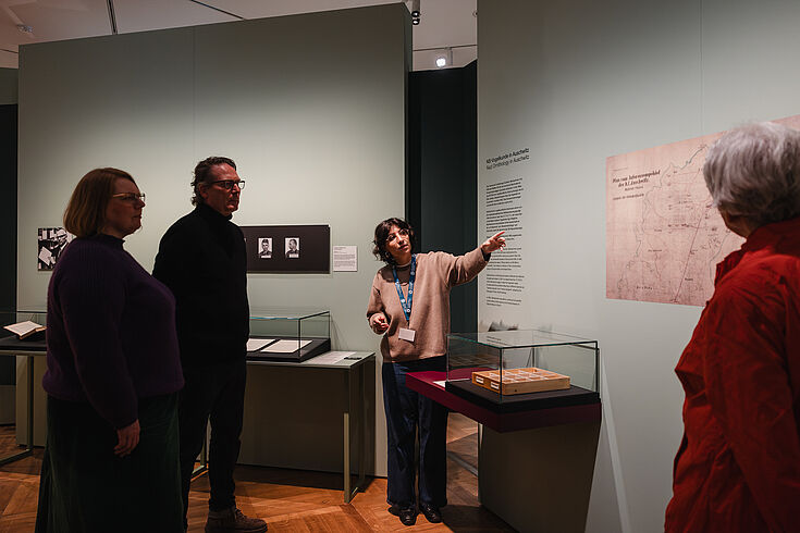 Mehrere Personen stehen in einer Ausstellung. Eine Person zeigt auf ein Objekt.