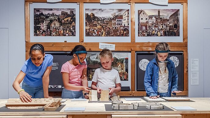Vier Kinder betrachten Objekte auf einem Tisch.