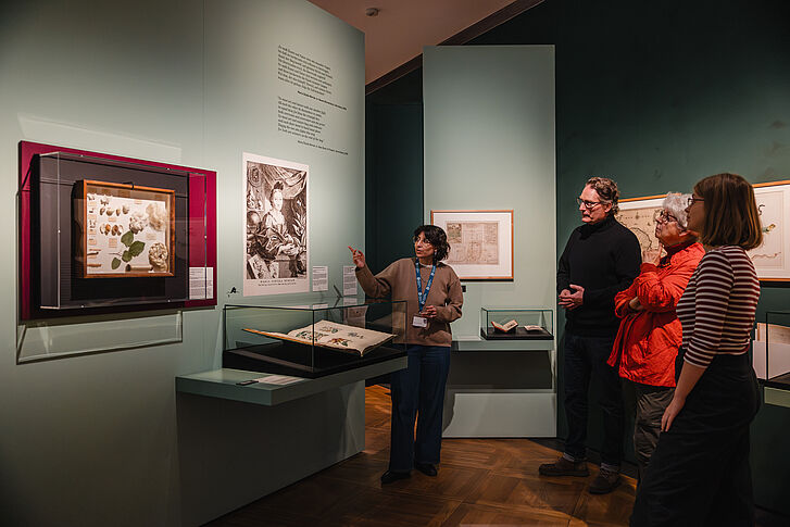 Exhibition view "Nature and German History. Faith – Biology – Power" A woman in a beige sweater gives three visitors a tour.