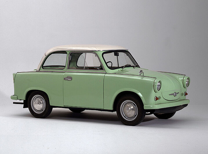 „Trabant P 50/2“,1962. Die seit Mitte der 50er Jahre entwickelten Trabant-Typen hatten eine Duroplast-Kunststoffkarosserie, da die traditionell im Autobau verwendeten Tiefzieh-Bleche gegen teure Devisen aus dem Westen hätten importiert werden müssen. 1962 kosteten die liebevoll „Rennpappe“ genannten Wagen zwischen 7.400 und 9.500 Mark. Damit entsprach der niedrigste Kaufpreis dem durchschnittlichen Jahreseinkommen eines Industriefacharbeiters. In den 60er Jahren mussten Käufer rund 6 Jahre auf die Auslieferung ihres „Trabi“ warten. Er wurde bis 1990 nahezu unverändert produziert und erreichte eine durchschnittliche Lebensdauer von 28 Jahren. (Inv.Nr. HI 90/14)