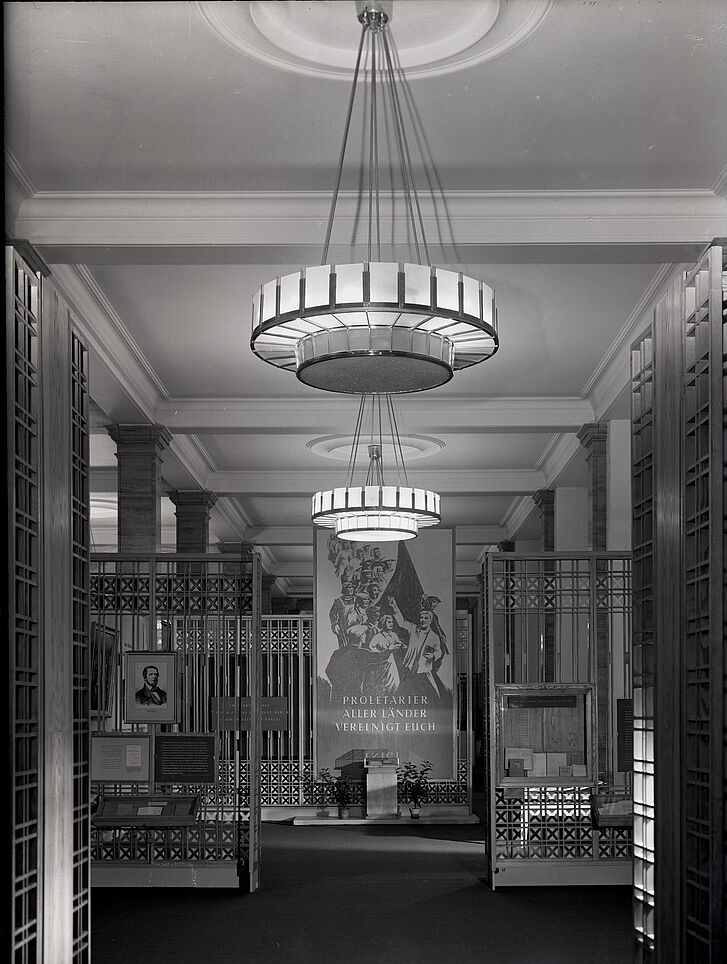 Exhibition view with pendant lamps and a poster